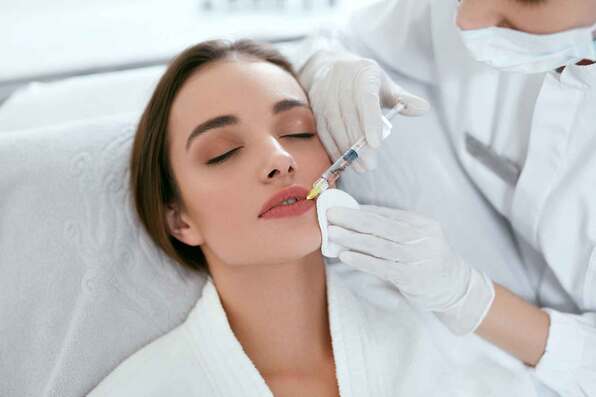 Image of a dark haired woman getting an injection in her lip from a medical provider 