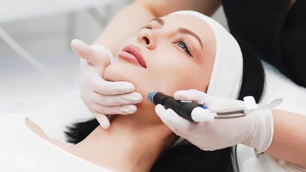 young woman getting a hydrafacial from a medical professional wearing gloves 