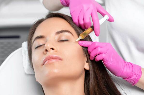 woman with dark hair receiving a facial injection from a medical provider in pink gloves 